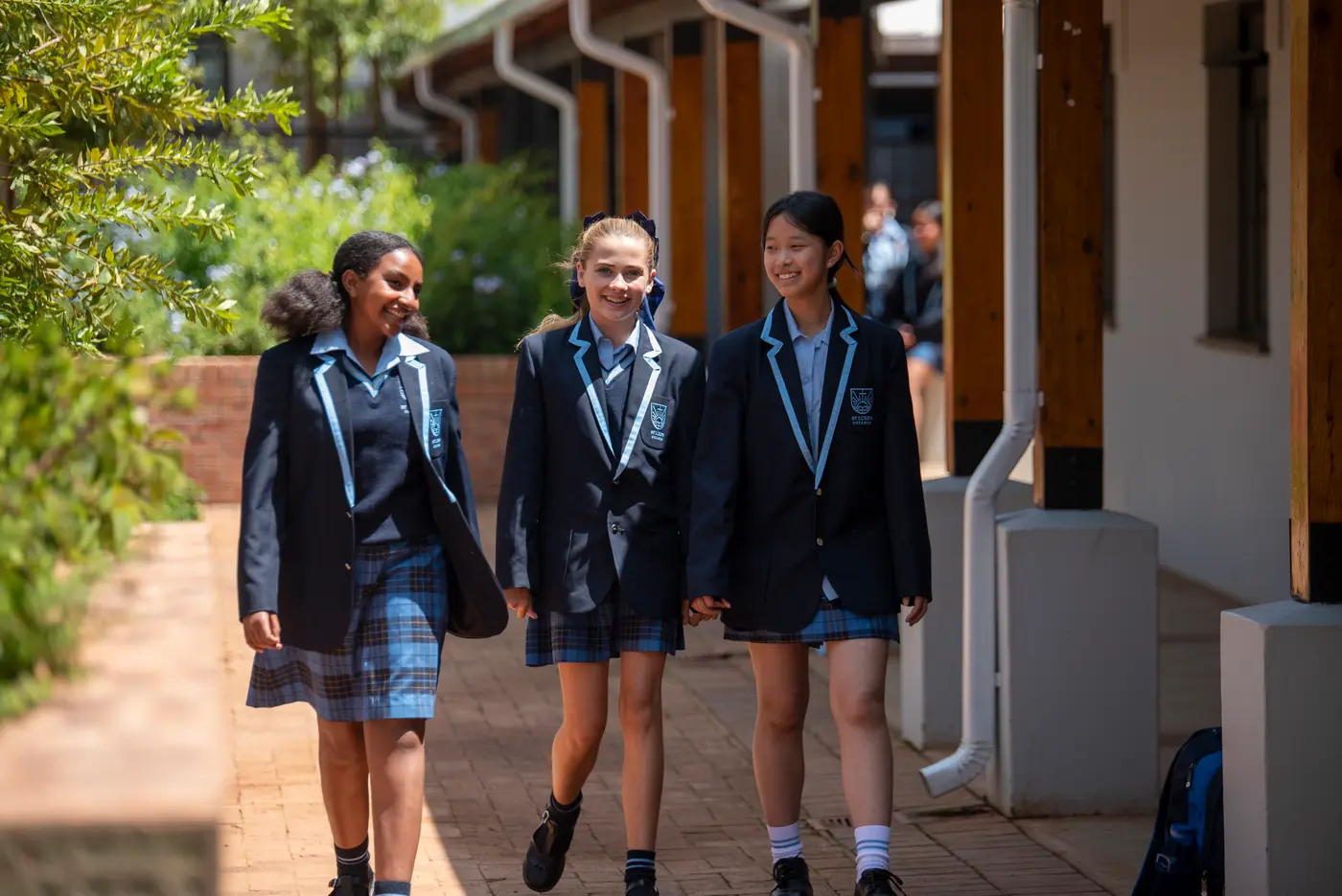 Three High School students in blazers walking and talking along a covered walkway